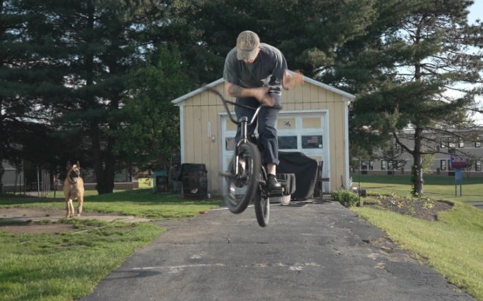 Billy Kennedy doing a bunnyhop barspin with his belgian malinois in the background